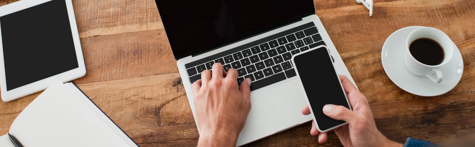 website developer holding smartphone while typing on laptop